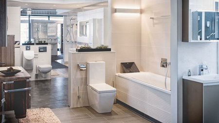 Ausstellungsbad mit eingebauter Badewanne, wandhängendem WC, hellen Wandfliesen und modernem Beleuchtungskonzept.