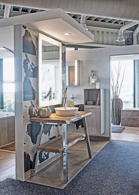 Modernes Badstudio mit freistehendem Waschtisch aus Naturholz, rundem Aufsatzbecken, beleuchtetem Spiegel und dekorativen Wandfliesen in graublauen Akzenten.